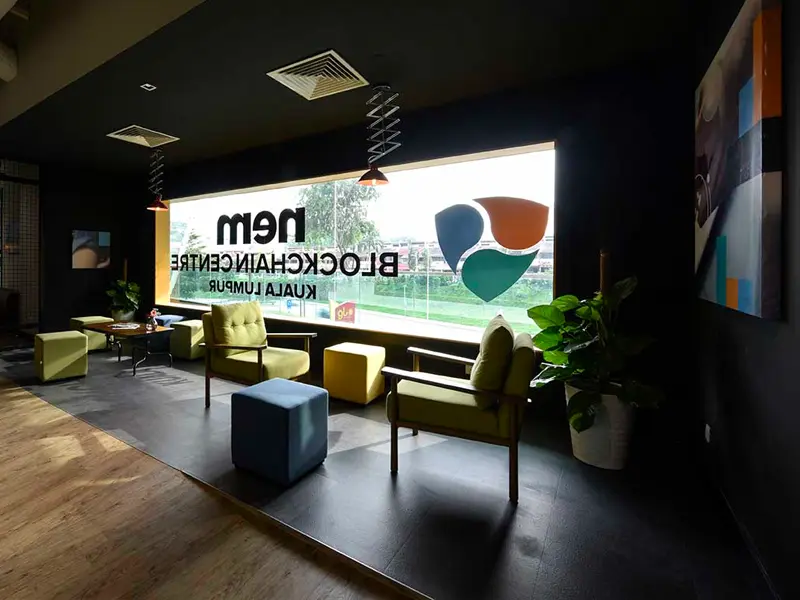 Interior of the NEM Blockchain Centre in Kuala Lumpur, featuring modern furniture, a large window with the NEM logo, and a welcoming atmosphere.