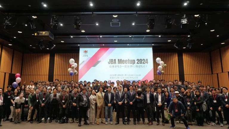Group photo of participants at the JBA Meetup 2024. The large gathering, held in a spacious conference room, showcases the extensive community involved in the event. The backdrop features a screen with the JBA logo and event details.